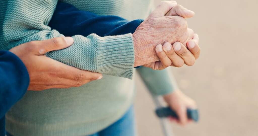 team member assisting resident by holding her hand