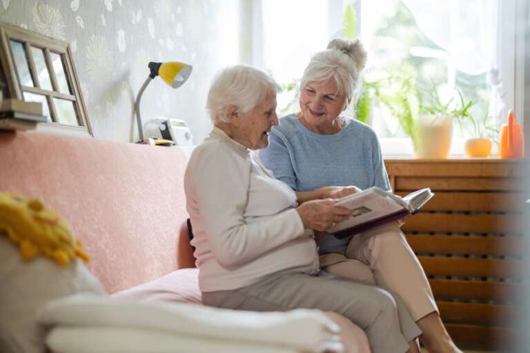 two older adults looking at photo albums on the couch